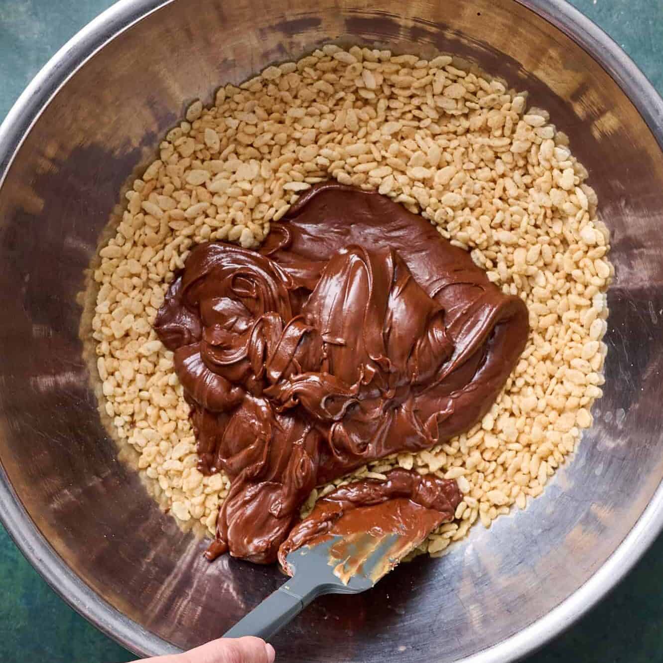 A large bowl with rice krispies cereal and the chocolate mixture added ready to be folded in