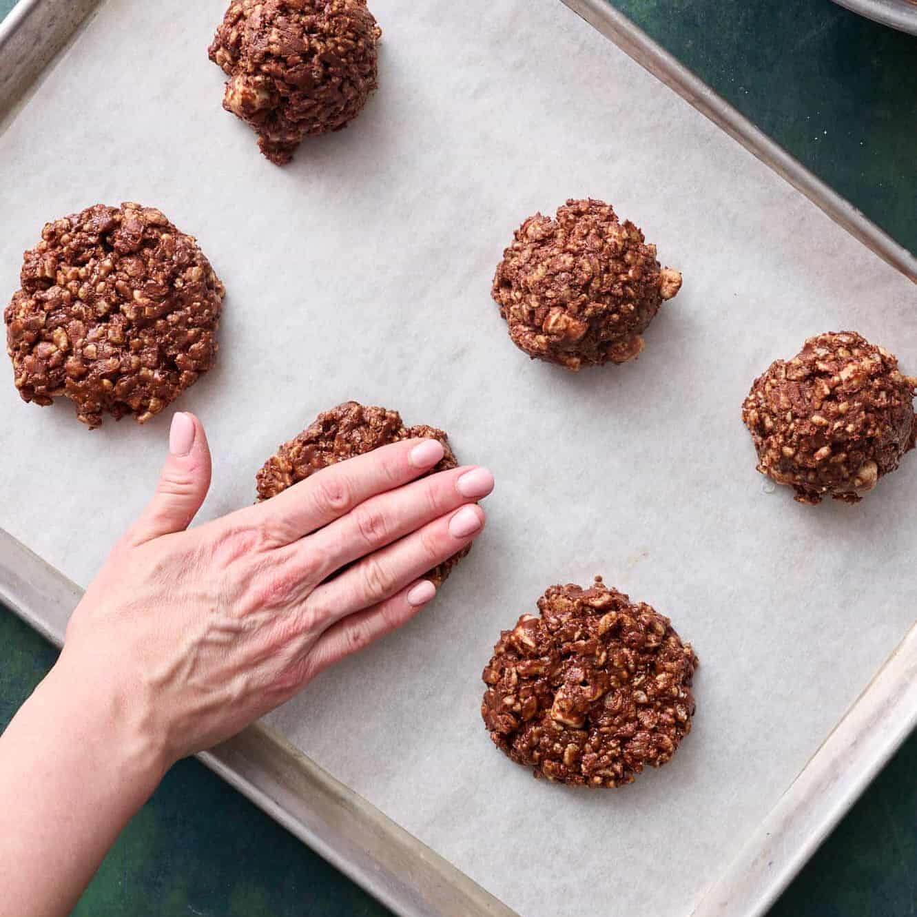 a hand smashing cookies down onto a sheet pan lined with parchment paper