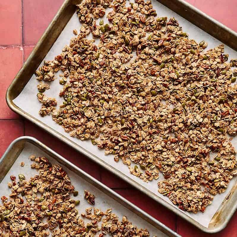 the granola mixture spread out on two parchment lined sheet trays