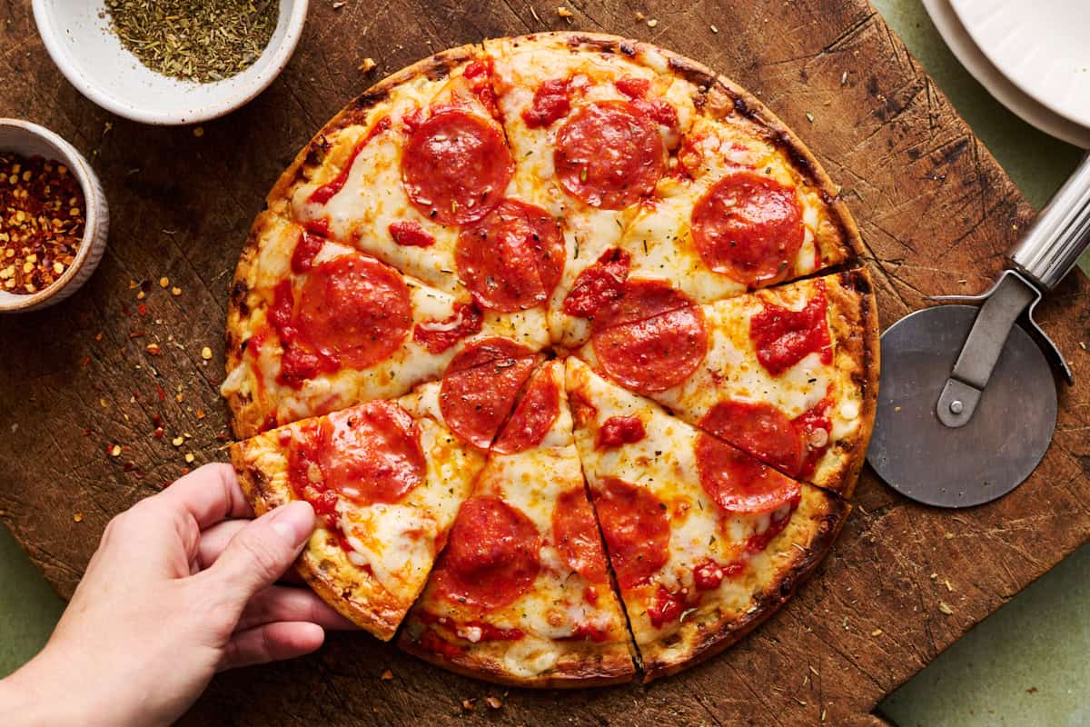 a sliced pizza with cottage cheese crust and a hand grabbing a slice