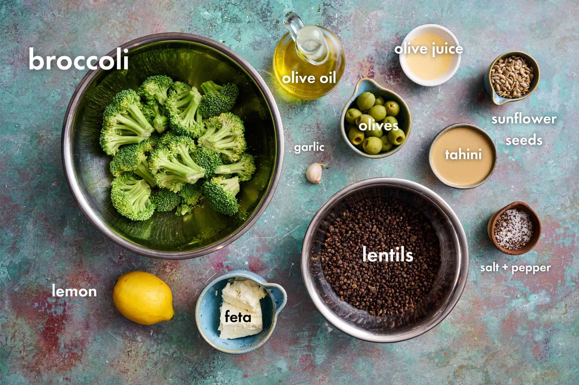 ingredients to make broccoli lentil salad including broccoli, lemon, tahini, lentils, feta and olives