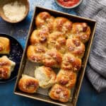 sourdough discard garlic knot rolls in a baking pan with marinara and parmesan