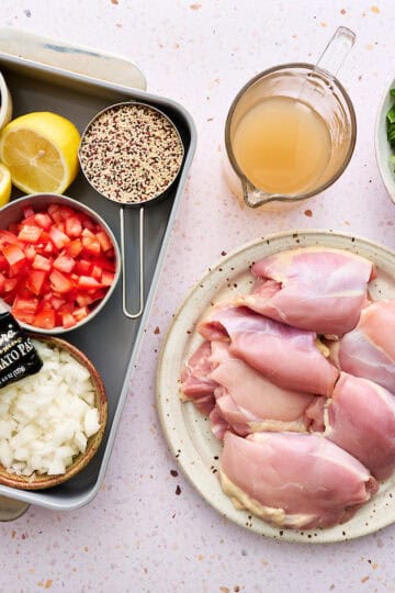 ingredients for this one-pan chicken bake including fresh spinach, chicken thighs, spices, garlic, broth, tomatoes, lemon, zucchini, onion, olives and feta