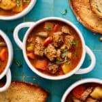 slow cooker beef stew in a white bowl with bread on the side