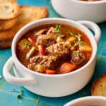 slow cooker beef stew in a white bowl with bread on the side