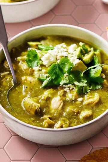 bowl of chile verde with chicken, cilantro and avocado with chips on the side
