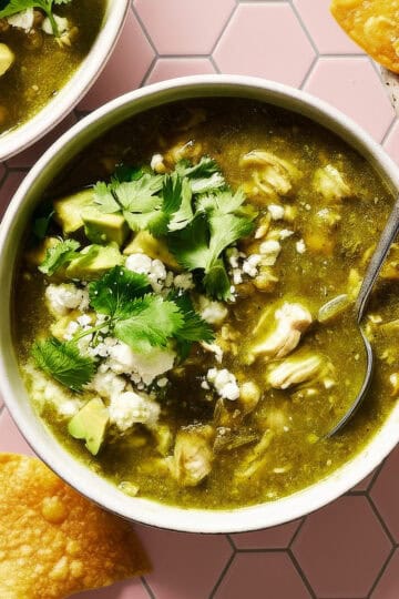 bowl of chile verde with chicken, cilantro and avocado with chips on the side