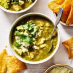 a bowl of chile verde topped with avocado, cotija cheese and cilantro with chips on the side