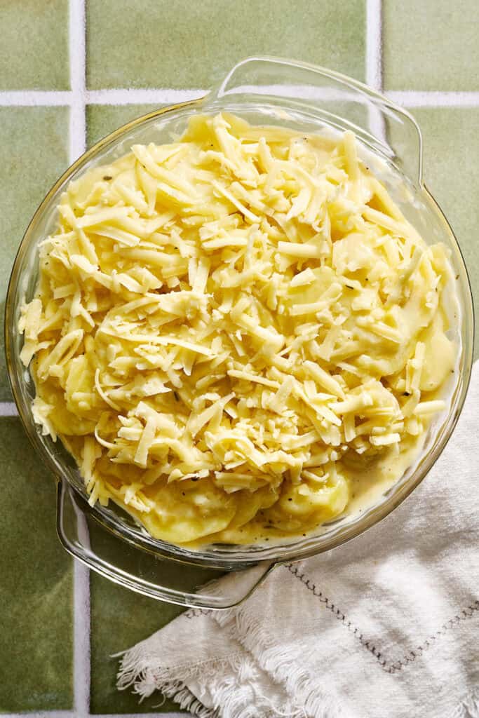 scalloped potatoes in a round glass baking dish topped with cheese before going under the broiler