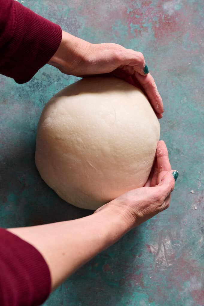 pulling the loaf of bread with two hands to create tension on the top of the dough