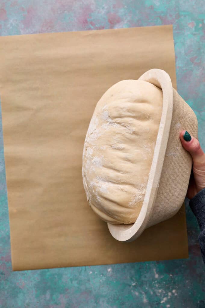 turning the proofed sourdough loaf out on to a piece of parchment paper from the proofing basket