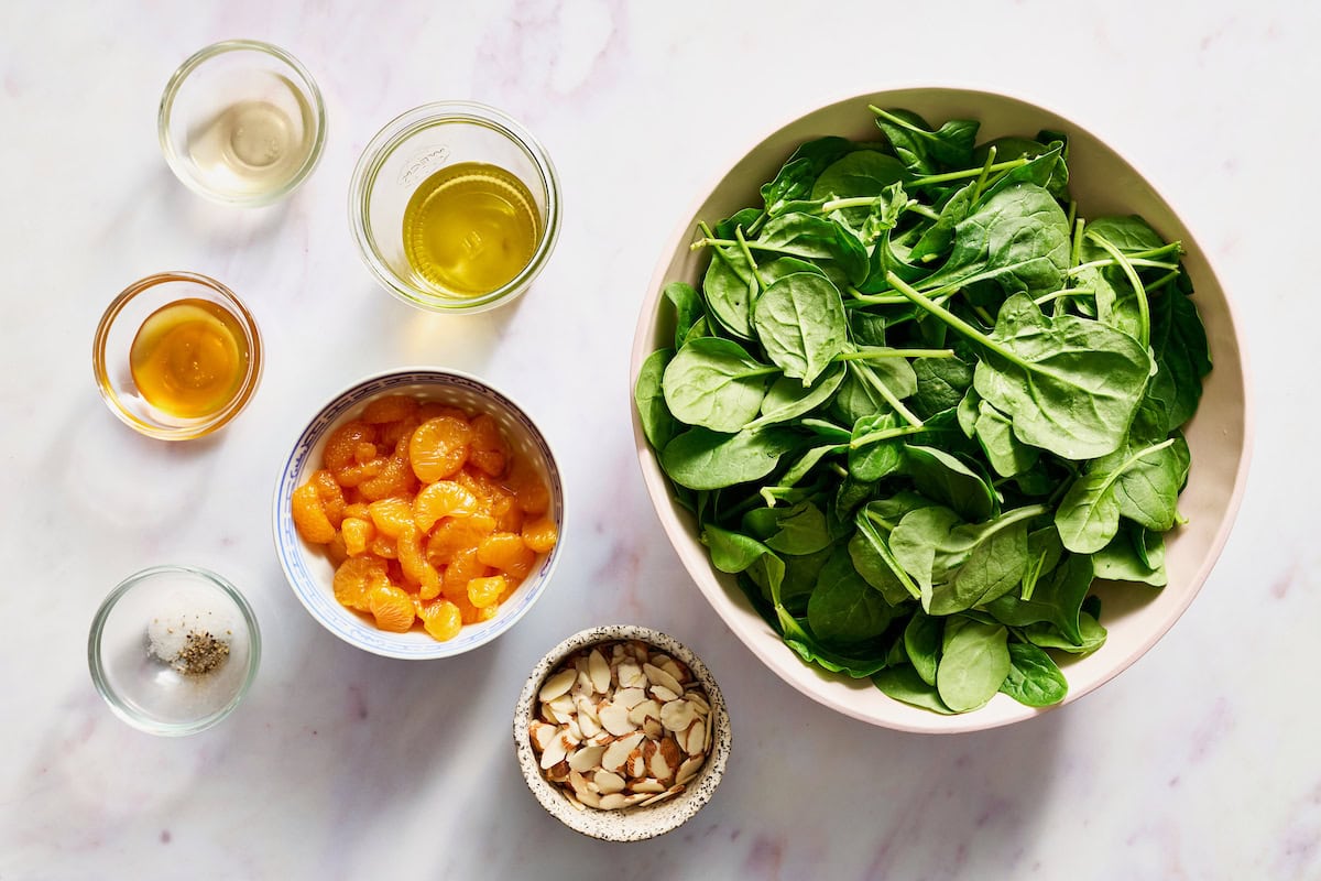 ingredients to make spinach salad with mandarin oranges including toasted almonds, oil, vinegar, honey, salt and pepper