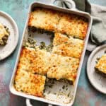 A large dish filled with a spinach, cheese and beef casserole with a piece taken out and put on a plate with a fork