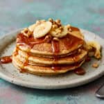 golden banana protein pancakes topped with syrup, banana and chopped walnuts