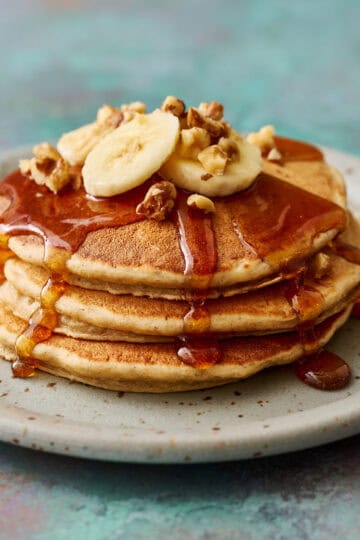 golden banana protein pancakes topped with syrup, banana and chopped walnuts