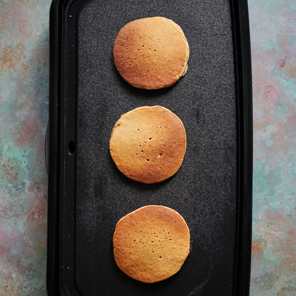 golden protein banana pancakes flipped on a griddle