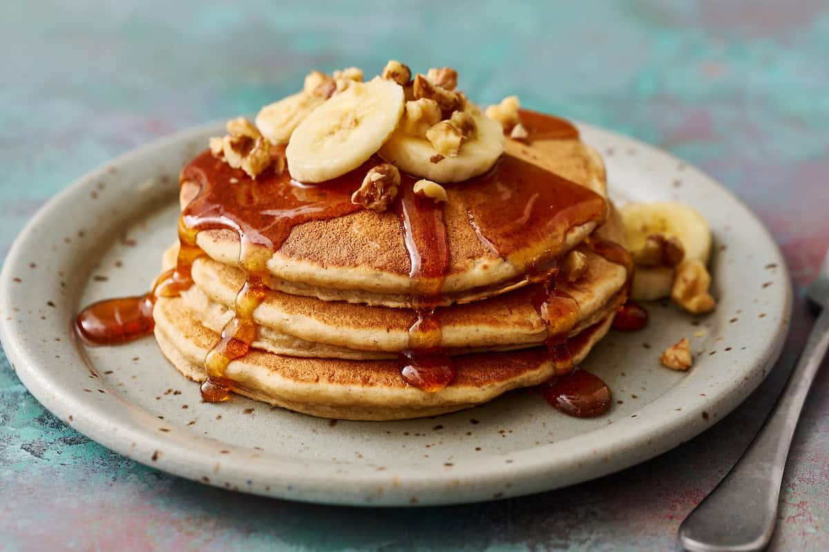 golden banana protein pancakes topped with syrup, banana and chopped walnuts
