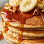 extreme closeup of golden banana protein pancakes topped with syrup, banana and chopped walnuts