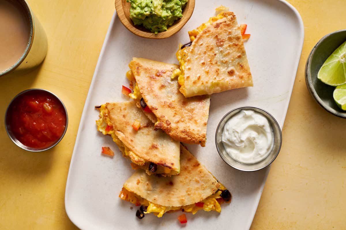 breakfast quesadillas served on a plate with greek yogurt, salsa and guac