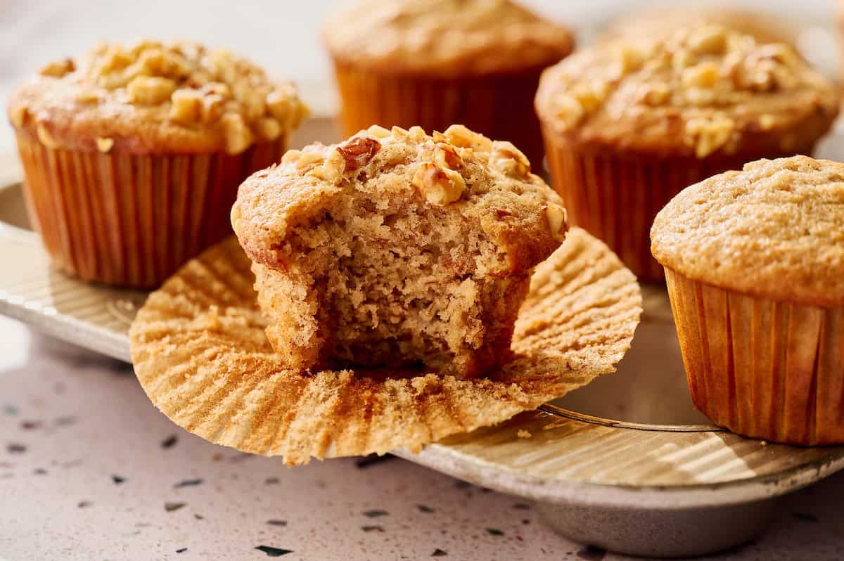 Sourdough discard banana nut muffins with golden domed tops and a bite taken out to show fluffy interior
