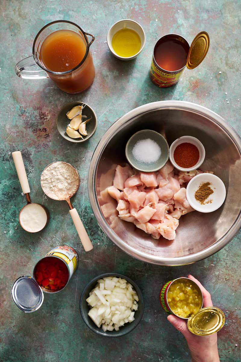 ingredients to make chicken enchilada soup including enchilada sauce, broth, garlic, masa harina, cream, rotel, chicken, spices, green chilies and onion
