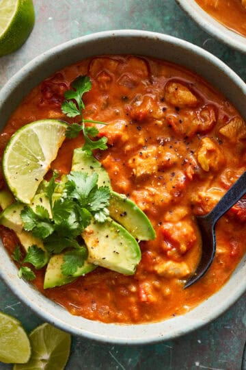 a bowl of chicken enchilada soup dressed with avocado and lime